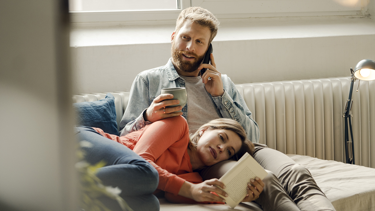 Un homme s’informe sur le modèle du médecin de famille en utilisant son téléphone, assis avec sa partenaire sur le canapé.